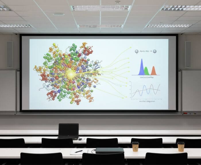 Conference room screen showing a molecular antenna complex diagram with excitation flow and spectral overlap graphics