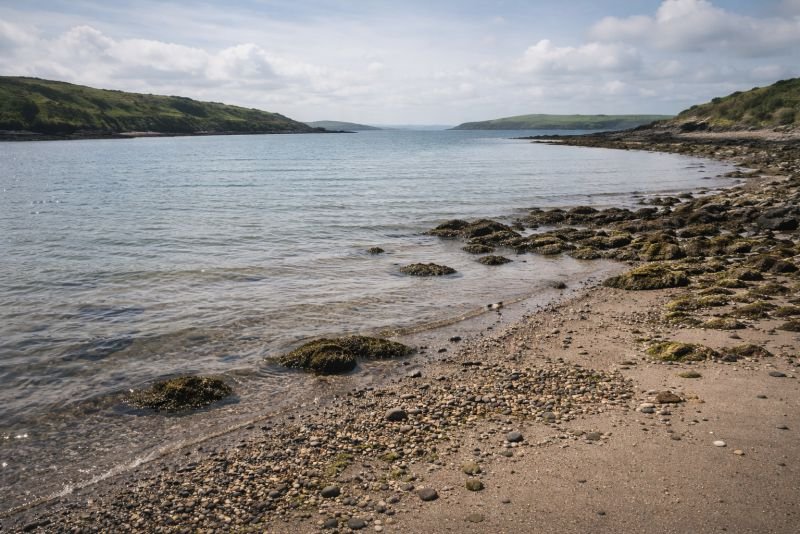 Coastal bay during neap tide with minimal water level change, calm sea surface and gently exposed shoreline under soft daylight.
