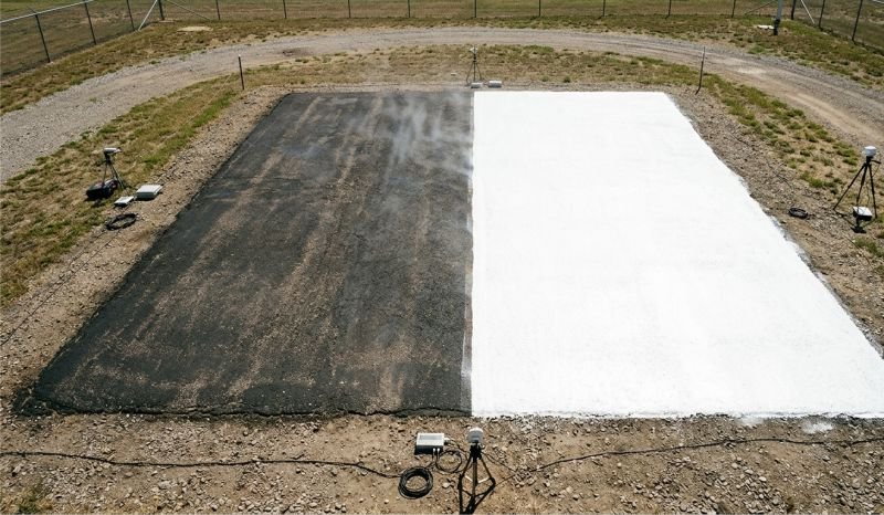 A photorealistic overhead view of two outdoor test surfaces under bright sunlight: a dark, textured asphalt pavement patch adjacent to a highly reflective white coating. Scientific measurement equipment is visible nearby.