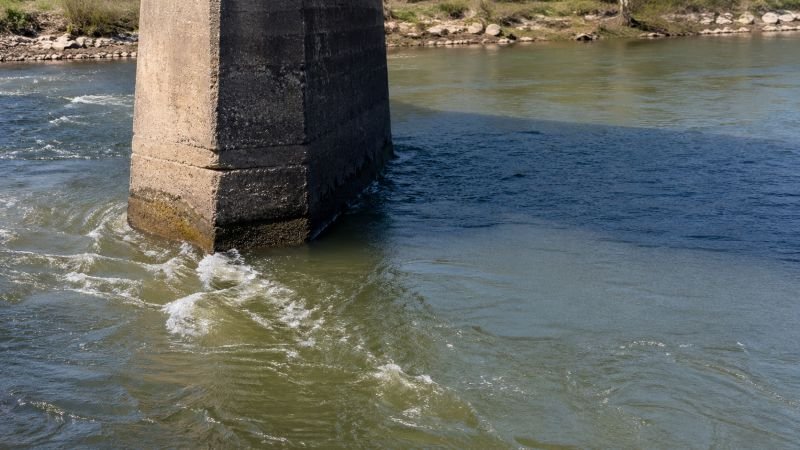 Bridge pier in moving river water showing visible flow separation and a calmer hydraulic shadow zone behind the obstruction.