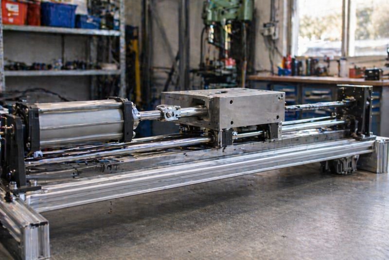 Mechanical work in physics and engineering shown by a linear actuator pushing a metal carriage along guide rails in a workshop test rig