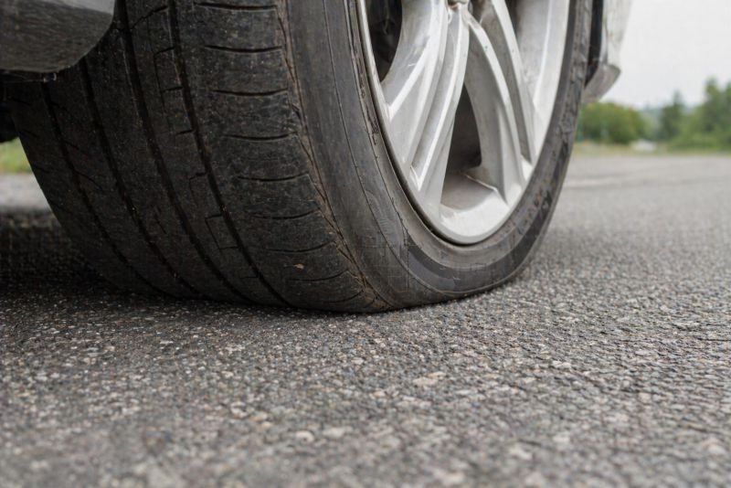 Close view of a vehicle tire rolling on textured asphalt with visible contact patch deformation illustrating rolling resistance in vehicle dynamics