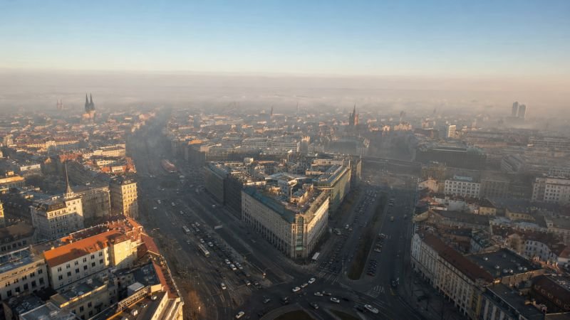Aerial view of a major city intersection with dense traffic and a visible haze layer at street level beneath clearer air above the rooftops
