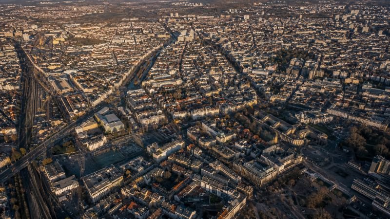 Aerial view of a dense European city with thousands of rooftops and facades, showing the scale of urban surface area available for atmospheric pollution dissolver deployment