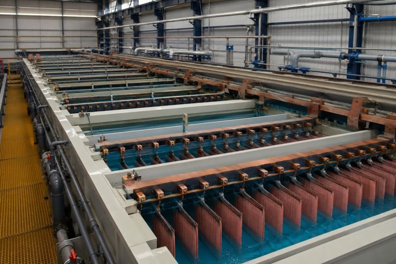 Industrial electrowinning tanks with suspended cathode and anode plates in blue electrolyte solution for copper recovery.