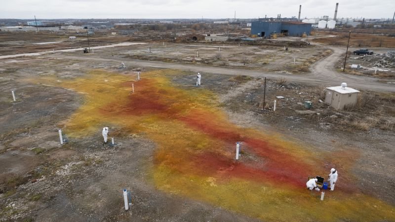 Brownfield remediation site with monitoring wells, field engineers in protective equipment, and a mapped groundwater contamination plume