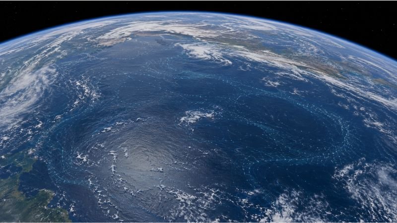 Earth seen from low orbit with a subtle network spread across major ocean gyres, showing ocean cleanup swarm infrastructure at planetary scale