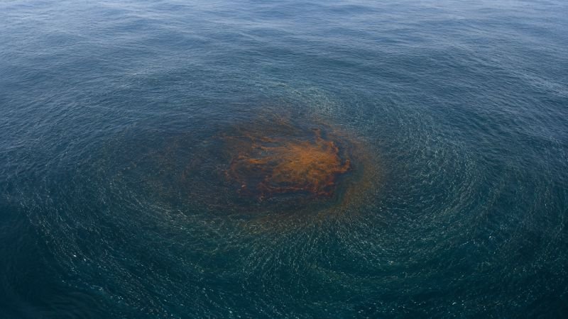 Open ocean surface with an orange oil contamination zone and a subtle converging swarm pattern showing self-organized cleanup coordination