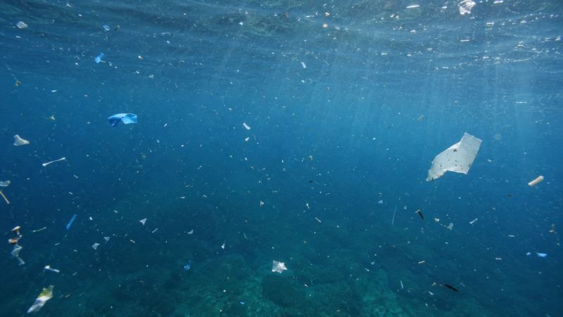 Open ocean water column with suspended white and blue microplastic fragments and natural particulates under filtered sunlight