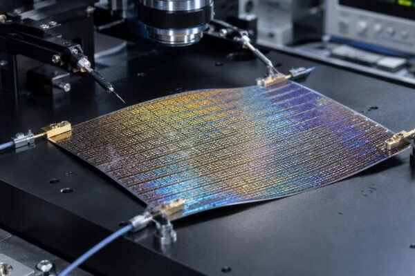 Quantum flux energy harvester film with iridescent rectenna grid, probe contacts, and microelectronics testing equipment on a dark laboratory bench