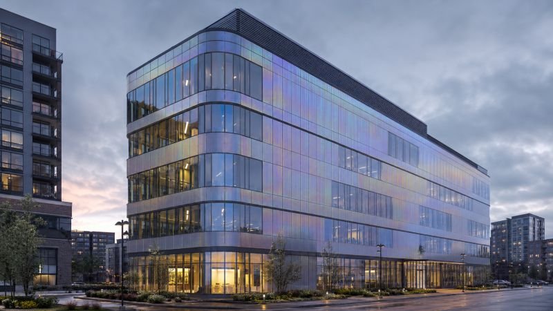 Modern commercial building with quantum harvesting film integrated across the facade, showing subtle iridescent energy-collecting surfaces at dusk