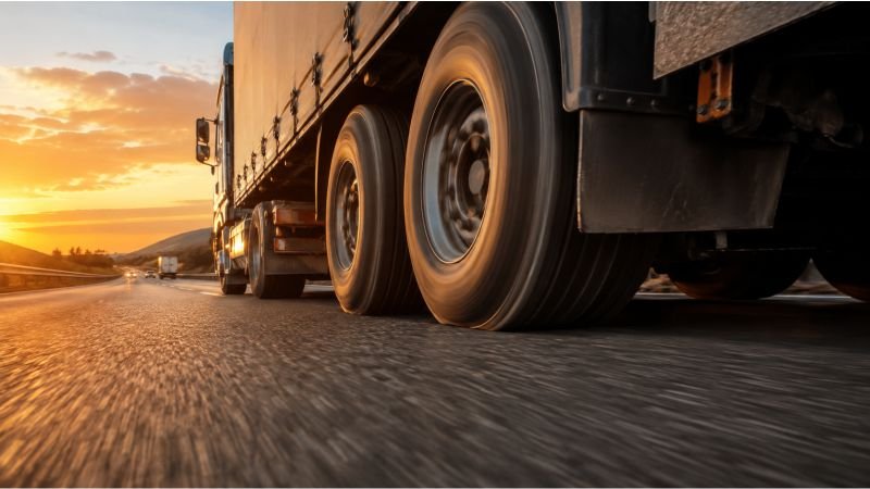 Heavily loaded freight truck at road level with tyres in motion, showing the rolling resistance energy loss built into wheel-based transport