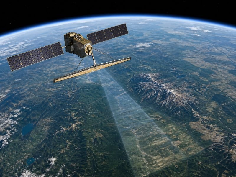Synthetic aperture radar satellite in low Earth orbit imaging terrain below for microwave remote sensing and surface mapping.