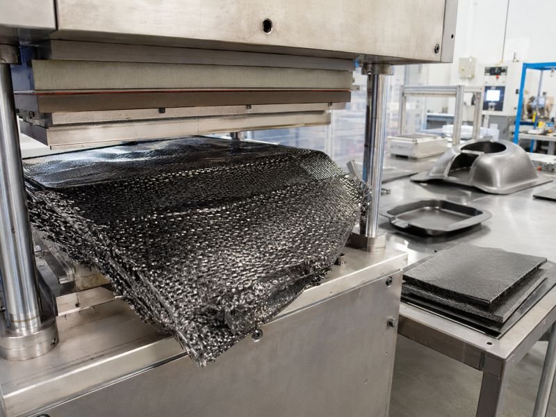 Thermoplastic composite fabric with woven fiber reinforcement being formed under a heated press in a clean manufacturing lab.
